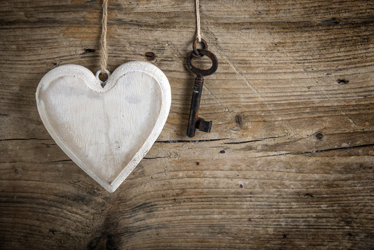 Heart from white painted wood and an old key hanging on a rustic wooden wall, love concept
