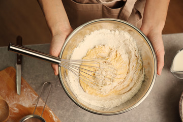 Young woman making dough in kitchen