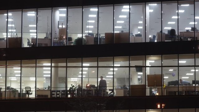 People work in skyscraper at night. Glowing windows of office building. The camera moves away from the object . Timelapse.