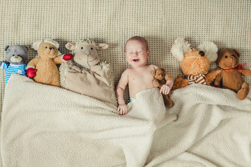 Happy boy lying with many plush toys under the blanket