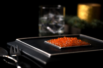 red caviar lies on a square ceramic stylish black plate