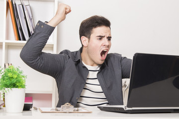 young man celebrating enthusiastically in front of laptop computer