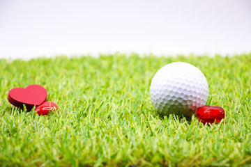 Naklejka premium golf ball and red heart are on green grass