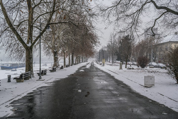 Frozen pathway in the park by the river on a snowing winter day