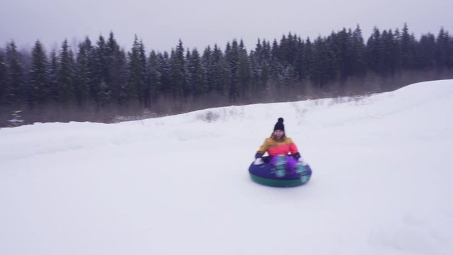 Young woman in bright winter clothes sliding on tube at Park on slopes of ski resort
