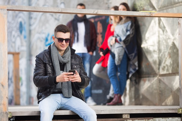 Fototapeta na wymiar Young man using his smartphone and sitting outdoors