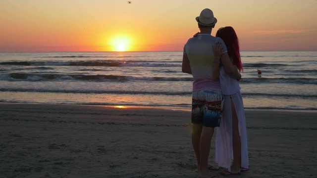 Couple hugging and kissing on the shore of a sandy beach at sunset