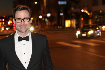 Sexy man in tuxedo and bow tie posing in the city streets at night