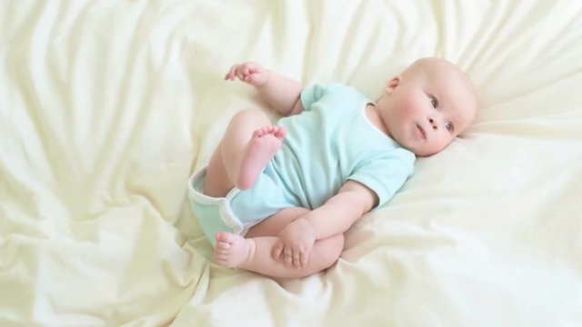 Little baby in a light blue bodysuit holding his feet.