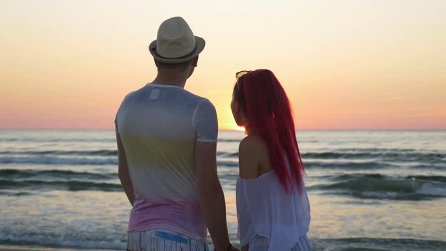 Young beautiful couple watching an amazing sunset and kissing on beach