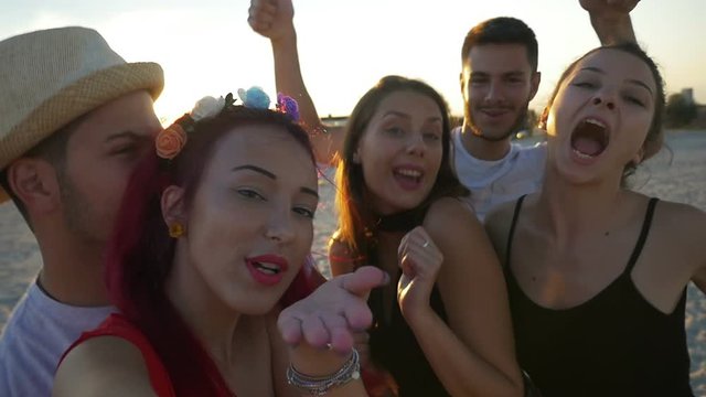 Group of friends taking selfies on the beach at sunset