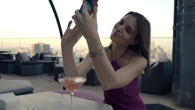 Happy woman taking selfie photo with cellphone sitting on terrace in bar 
