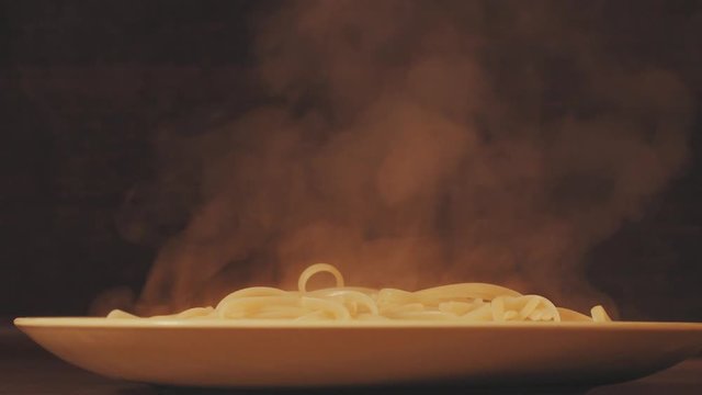 Hot spaghetti putting on a plate, sprinkling with cheese and adding tomato sause