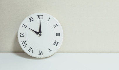 Closeup white clock for decorate show 10 a.m. on white wood desk and cream wallpaper textured background with copy space