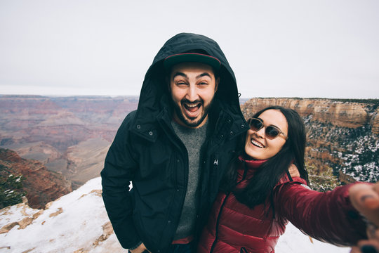 Romantic multiracial couple show thumbs up and make selfie photo on travel hiking at Grand Canyon viewpoint in winter, Arizona, USA