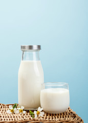 A bottle of milk and glass of milk on a wicker table on a blue b