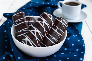 Fragrant cookies of choux pastry in dark chocolate covered with white decoration  and cup of coffe on blue napkin on a white background. Close up