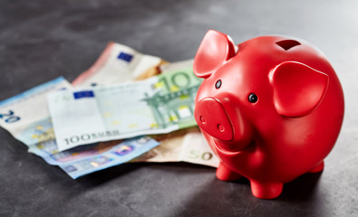 Red piggy bank and Euro banknotes on gray surface