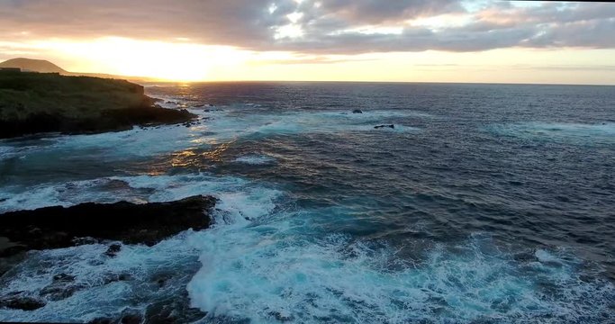 Aerial shot of sunset in the ocean with rocks and foam. Epic view in the evening sea.