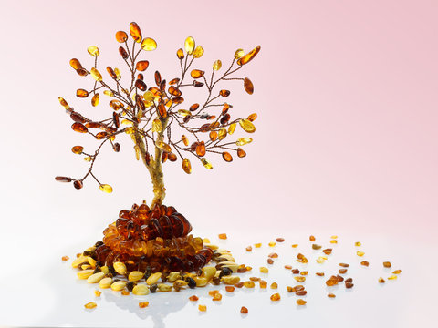 Decorative tree made with&nbsp;yellow and dark brown baltic amber, amber beads and small pieces of raw amber on white acrylic surface on pink gradient background