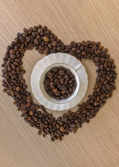 Coffee cup and coffee beans on a wooden table and heart shape made from coffee beans