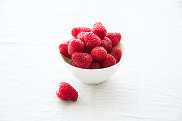 Fresh raspberries in a big red ceramic bowl on a white table.