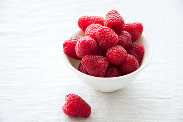 Fresh raspberries in a big red ceramic bowl on a white table.