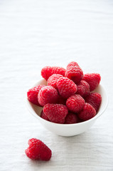 Fototapeta na wymiar Fresh raspberries in a small white ceramic bowl on a white table