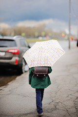 Kid girl with umbrella walking in city street