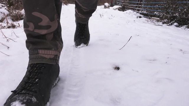 Man walking in winter snow, leather boots making fast steps towards low angle camera in motion