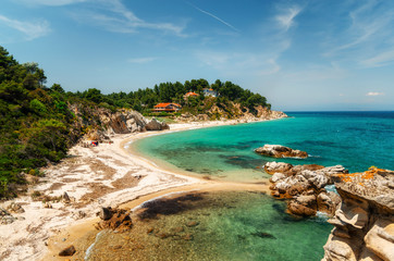 Wild beautiful beach with turquoise water, fine sand and large stones in Vourvourou. Pine trees on the shore, Sithonia, Greece