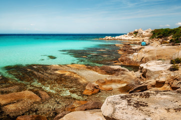 Wild beautiful rocky beach with turquoise transparent water and large stones in Vourvourou, Sithonia, Greece