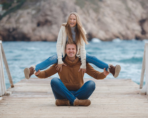 Fototapeta na wymiar A couple in love,young woman in a white knitted sweater,long blond hair and a young man with short blonde hair,the girl sitting on the shoulders of the guy on the background of sea and mountains 