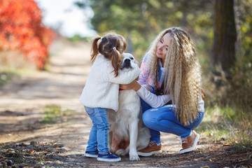 Fototapeta premium Family portrait of young blonde woman with long wavy hair and her little daughter,walking together with the dog breed Golden Retriever in a beautiful autumn Park