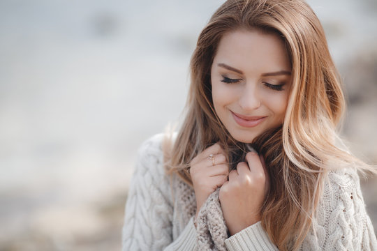 Fototapeta Spring portrait beautiful woman with blond, long,straight hair,large black eyelashes,wearing jewelry,wearing a knitted sweater is white with a large beige collar,posing outdoors