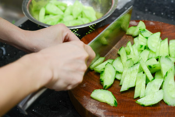 lady preparing cucumber slices on a wooden chop board