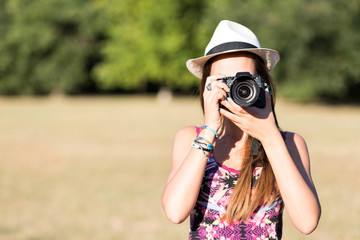 beautiful brown hair girl with white panama hat while shooting a picture with her camera at park in a sunny day. summer portrait