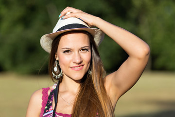 Beauty Romantic Girl Outdoors. Beautiful young brown hair model holding a white panama hat at park in Sun Light. Summer portrait. Glow Sun, Sunshine.