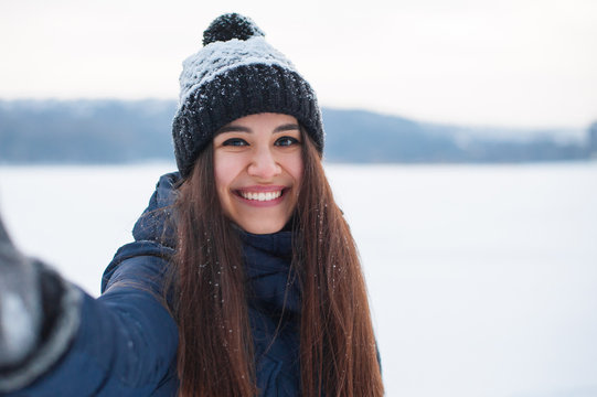 Young beautiful woman taking selfie photo in winter snow park near frozen lake
