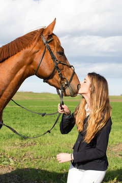 Beautiful girl dressing uniform competition kiss her horse on the grass: outdoors portrait on sunny day