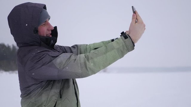 man makes selfie, choose a convenient angle, against the backdrop of snow-covered lakes and forests, 4k