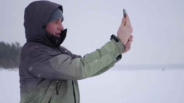 man makes selfie, choose a convenient angle, against the backdrop of snow-covered lakes, forests and kitesurfing, 4k