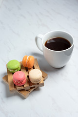 Sweet and colourful macaroons served on little wooden pallets with cup of coffee on a marble texture background. Traditional french dessert. Copy space.