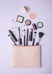 Aerial view of a pink make up bag, with cosmetics spilling out on to a pastel purple background