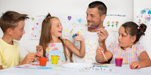 Portrait of a cute happy father with children painting and having fun. They are showing their hands painted in bright colors