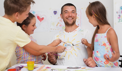 Portrait of a cute happy father with children painting and having fun. They are showing their hands painted in bright colors