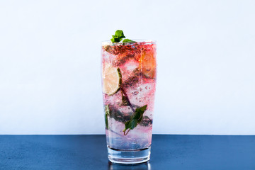 Fresh strawberry Mojito cocktail with lime, fresh mint and ice in high glass on a wooden table.
