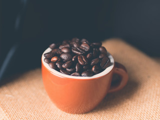 Coffee beans in italian espresso cup on burlap and dark blue black background