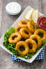 Fried calamari rings with lettuce and ketchup on wooden background
