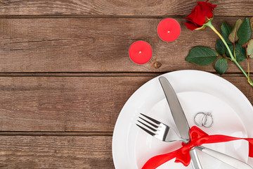 Valentine's Day dinner table setting with red ribbon, rose, knife and fork  ring over oak background.